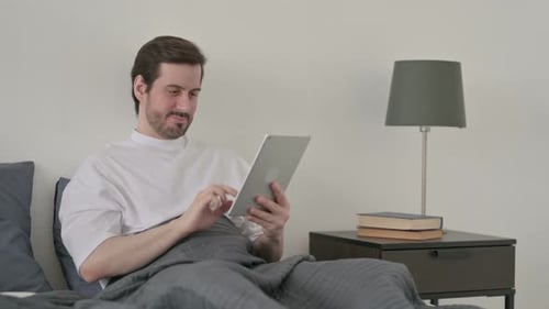 Man Relaxing in Bed Using Tablet