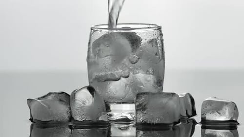 Water Being Poured Over Ice in Clear Glass