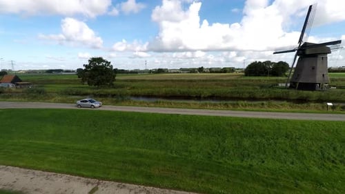 Silver Car Driving Alongside Canal with Windmill