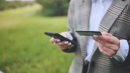 A Young Business Lady Makes a Purchase with Her Phone and Bank Card in the Park
