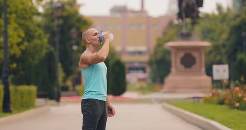 Athletic Man Drinks Water in Urban Park