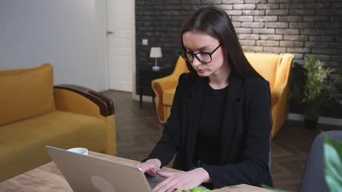 Müde hübsche kaukasische Geschäftsfrau mit Brille tippt auf Laptop und arbeitet im Home Office