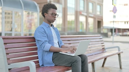 Young Adult Using Laptop on Bench Outside