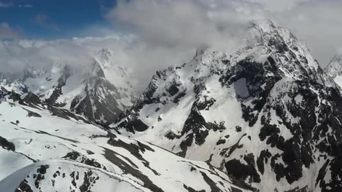 Air Flight Through Mountain Clouds Over Beautiful Snowcapped Peaks of Mountains and Glaciers