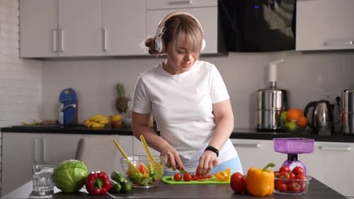Woman With Headphones Prepares a Salad in Kitchen