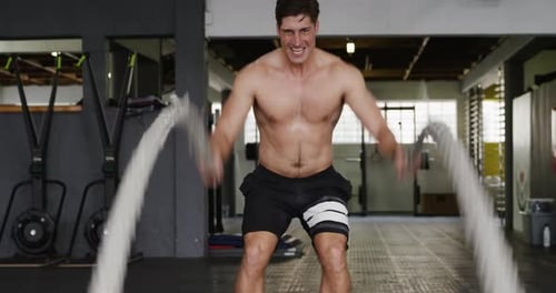 Front view athletic Caucasian man working out with battle ropes