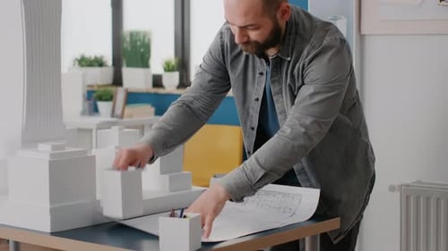 Close Up of Man Architect Analyzing Blueprints Plans on Table to Design Building Model