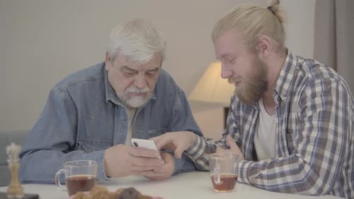 Senior Man and Young Adult Using Smartphone Together