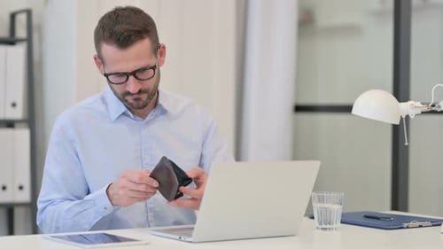 Mann mittleren Alters überprüft leere Brieftasche während der Arbeit am Laptop