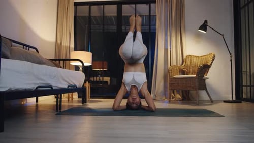 Woman Does Headstand Yoga Pose at Night Indoors