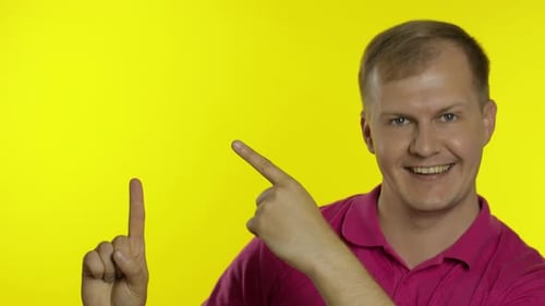 Portrait of Young Man Posing in Pink T-shirt. Happy Smiling Guy Pointing at Something with Hand