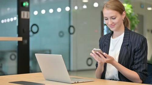 Professional Businesswoman with Laptop Using Smartphone in Office