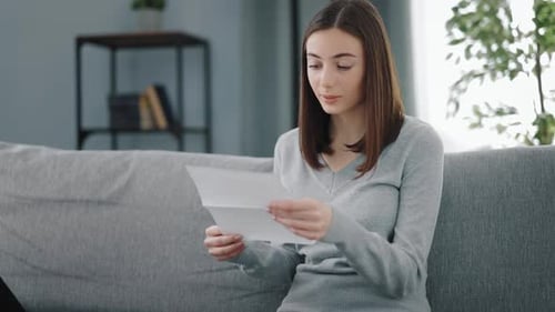 Happy Woman Reads Letter on Couch at Home