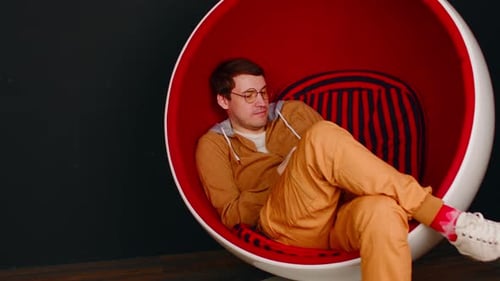 Jeune homme avec téléphone portable assis dans une chaise de bal sur fond noir