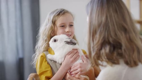 Child Holding Rabbit, Smiling at Adult Inside Home