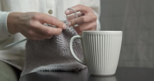 Woman Knitting With Needles Near a Mug Indoors