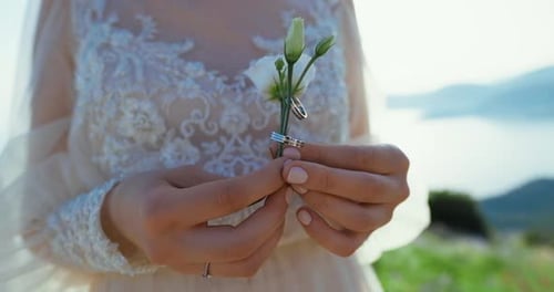 Close Up of Wedding Rings on Flower Held by Bride
