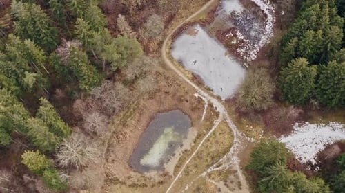 Flying a tight circle over frozen lakes in a conifer forest with pathes of snow in a smooth top down