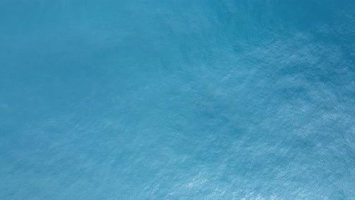 Texture water patterns and sunlight across a light blue ocean surface. Artistic drone capture