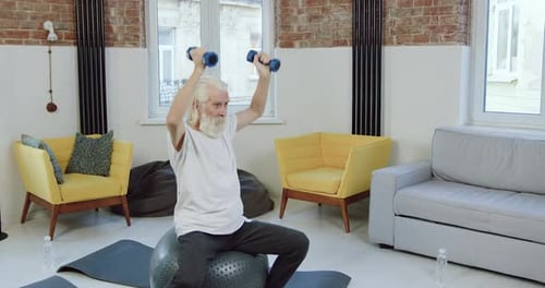 Senior Man Lifts Weights While Sitting on Exercise Ball