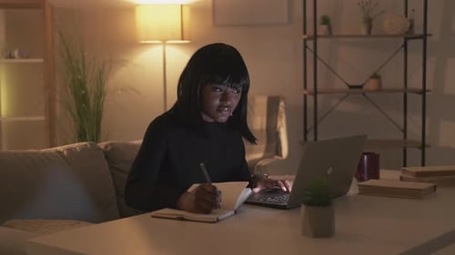 Woman Working on Laptop and Writing at Home