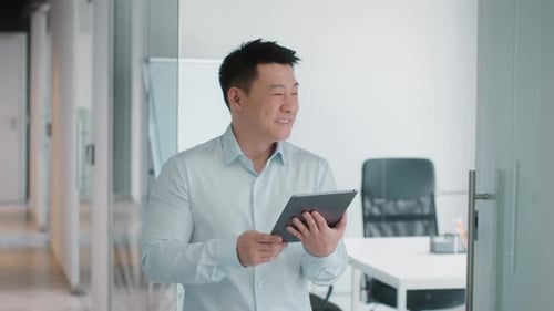 Positiver asiatischer Geschäftsmann mittleren Alters liest soziale Medien auf einem digitalen Tablet und lächelt im Büro