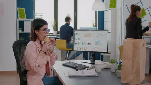 Woman Eating Sandwich While Working at Modern Office