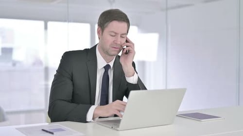 Businessman Talking on Smartphone While Using Laptop
