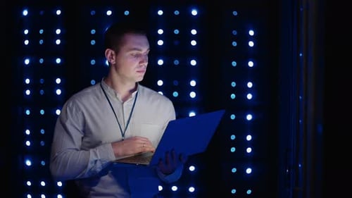 Young Man Working on Laptop in Dark Server Room