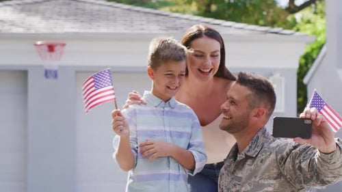 Happy caucasian male soldier taking selfie with smiling son with wife in garden outside their house