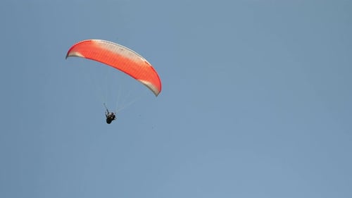 Red parachute flying against clear blue sky.
