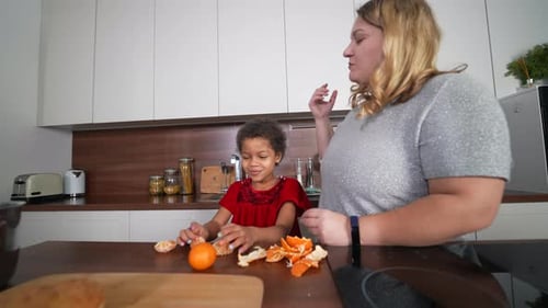 Child Peeling an Orange with Adult in Kitchen
