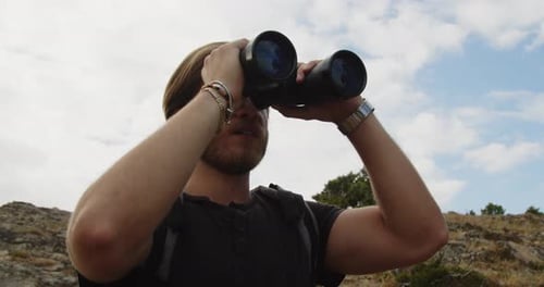 Man Hiker Using Binoculars on Sunny Hillside