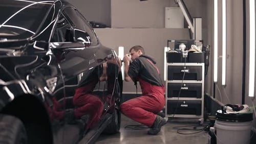 Technician Polishing Black Car in Auto Repair Garage