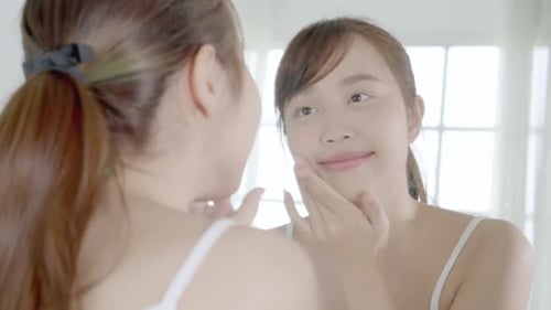 Woman Applying Cream to Face in Mirror