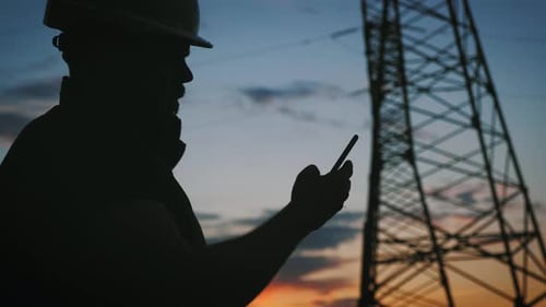 Silhouette of Engineer Standing on Field with Electricity Towers