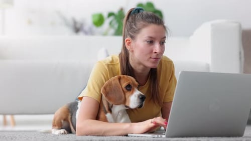 Studentin liegt mit Laptop auf dem Boden und macht Hausaufgaben mit Hund Spbi