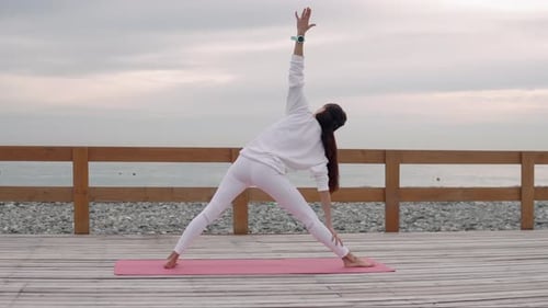 Une gymnaste féminine exécute le Trikonasana en plein air pendant une journée d'été près de la mer
