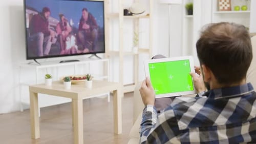 Man Touching a Green Screen Digital Tablet PC While Looking at the TV