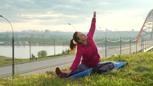 Woman Stretching on Grass Near City and Bridge