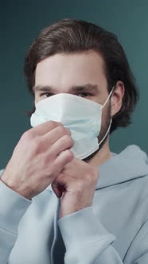 Encantador hombre de pelo oscuro vestido sudadera ligera con capucha puesta en una máscara facial protectora
