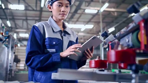 Engineer is using a tablet to check the machine's control system in a factory.