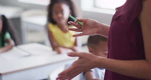 Video of midsection of caucasian female school teacher studying diverse children in classroom