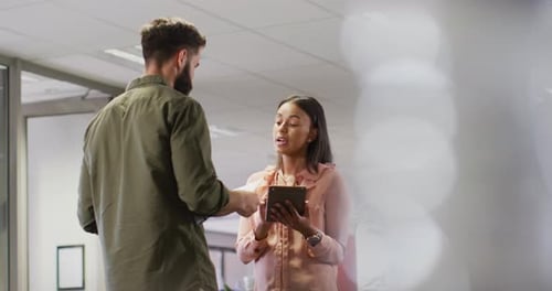 Video of diverse businesswoman and businessman using tablet and talking in office