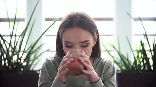 Young Woman Drinks Juice and Smiles Indoors