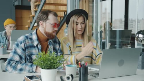 Colleagues Caucasian Man and Asian Woman Working Together Talking and Using Laptop in Office
