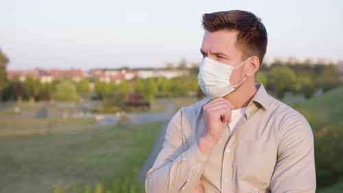 A Young Caucasian Man in a Face Mask Thinks About Something on a Town's Outskirts