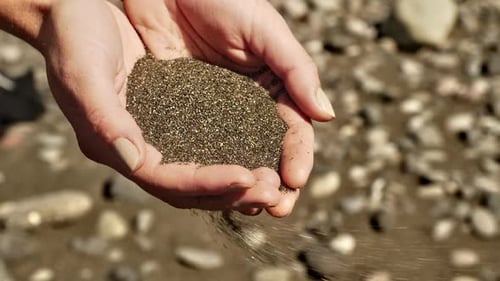 Hands Holding and Releasing Black Sand