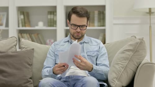Frustrated Man Reviews Papers at Home on Couch