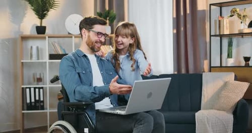 Papá discapacitado en silla de ruedas divirtiéndose junto con su hija de 10 años mientras usa la computadora